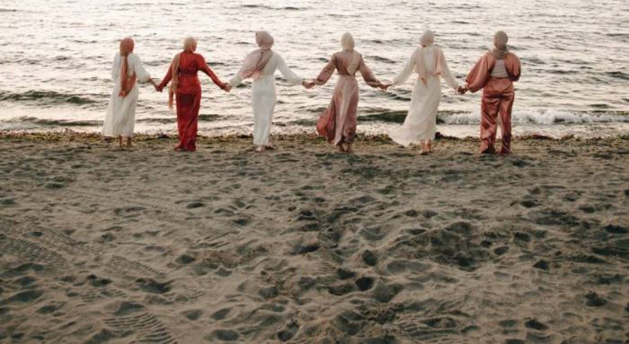 Circle of women holding hands on the beach at sunset, retreat ambiance